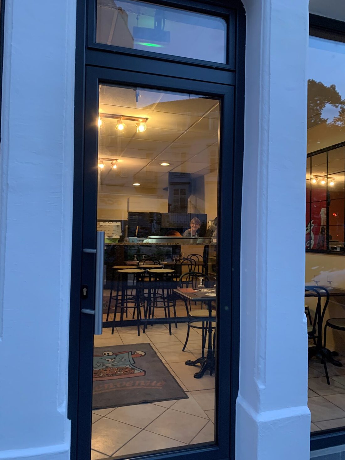 L’entrée de la pizzeria et la salle derrière la porte vitrée