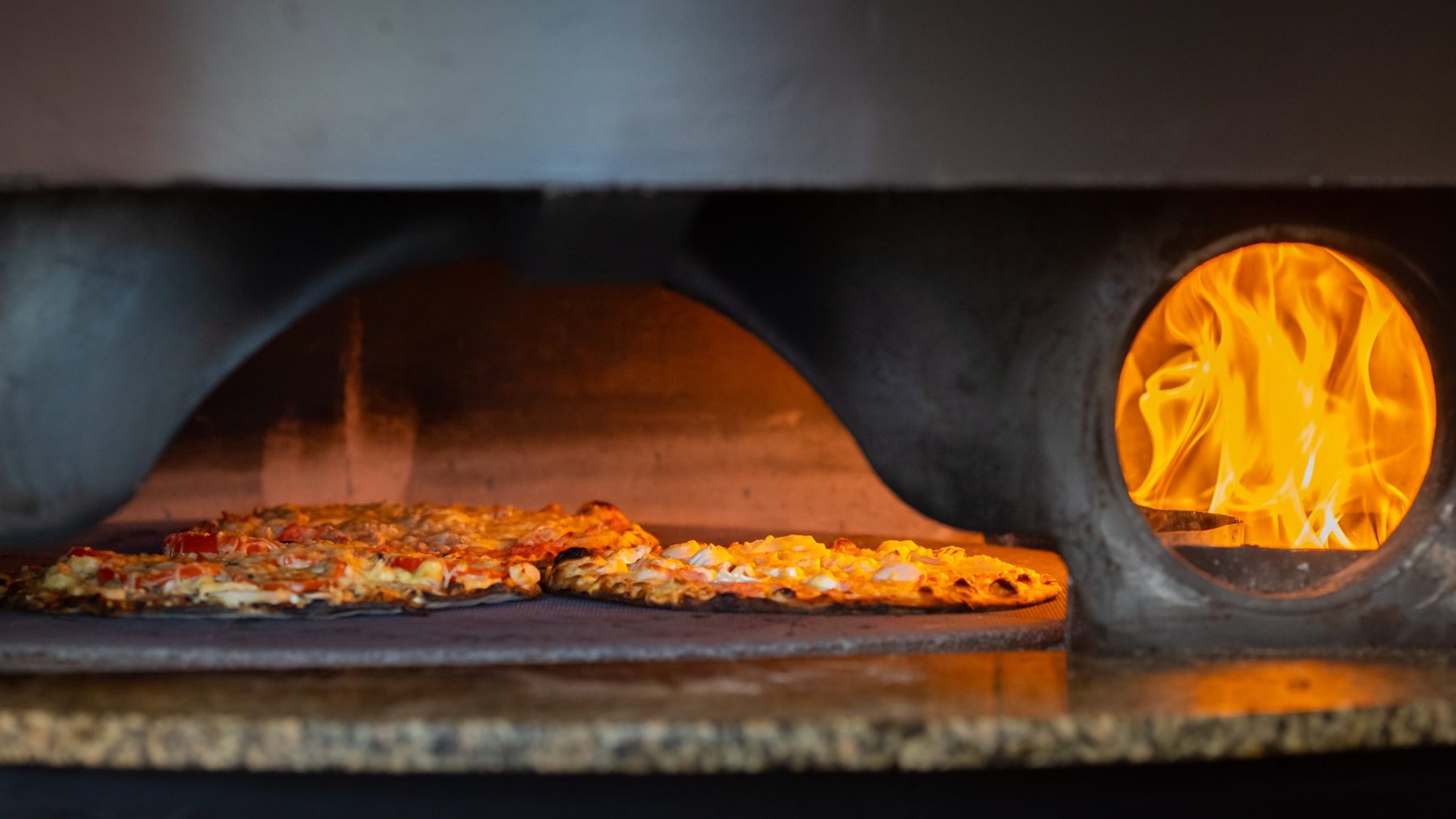 Une pizza au feu de bois dans le four, flammes au fond