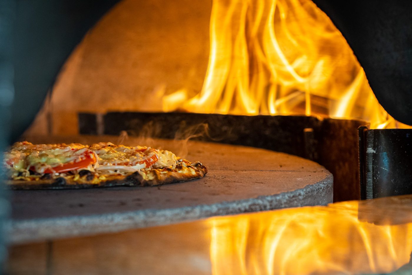 Une pizza sur la pierre du four, flammes derrière